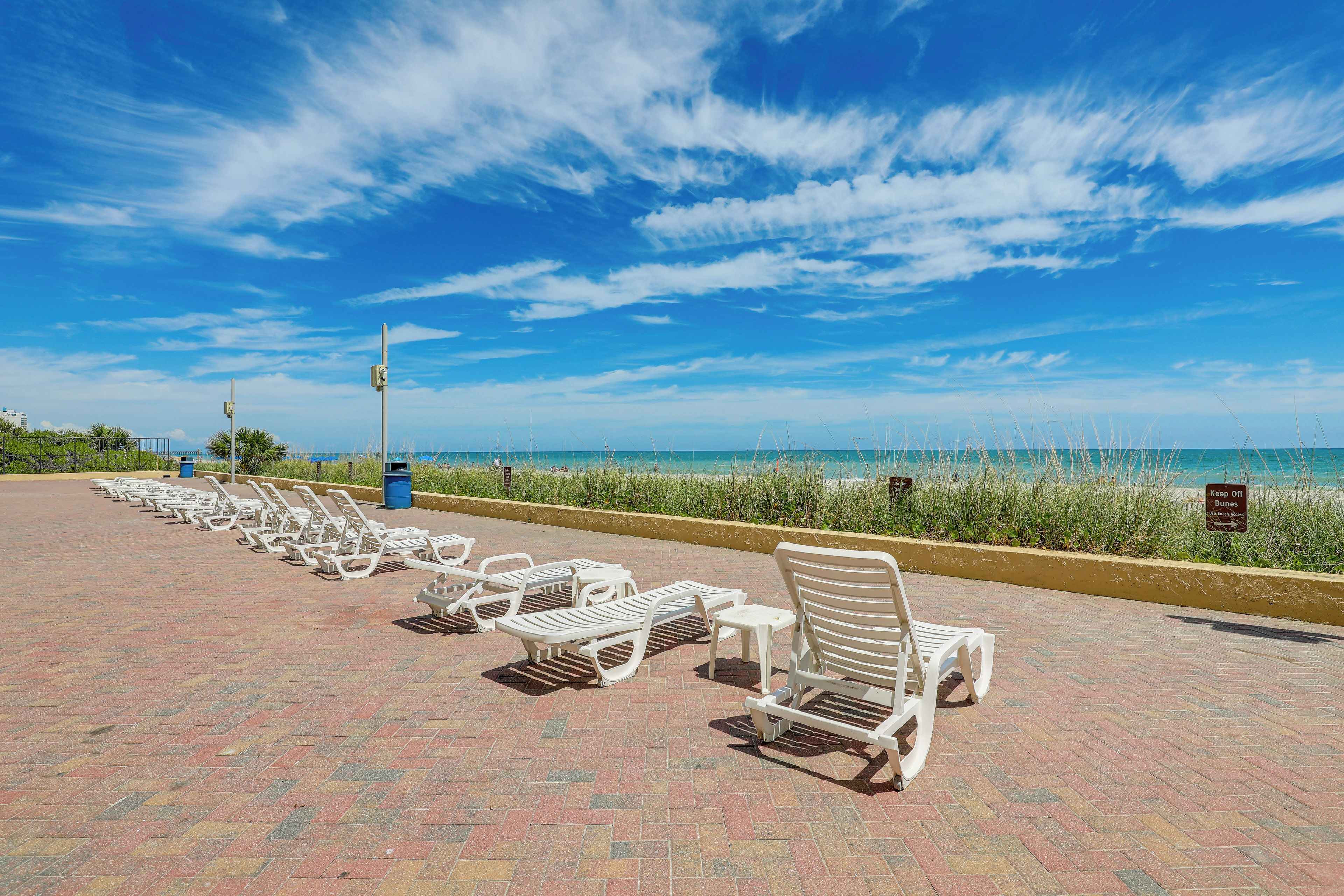 A beachside walkway with white lounge chairs and a clear view of the ocean.