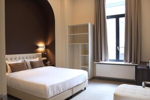 A bedroom with a large bed, a wardrobe, a nightstand, and a window with curtains.