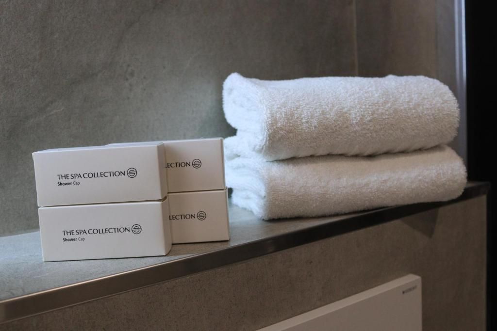 Een badkamer met een handdoek en drie dozen met de tekst 'The Spa Collection Shower Cap' op een plank.