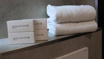 Een badkamer met een handdoek en drie dozen met de tekst 'The Spa Collection Shower Cap' op een plank.