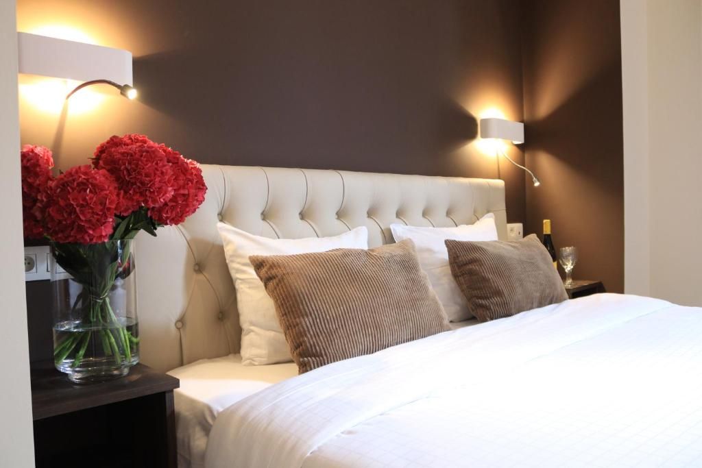 Een hotelkamer met een gestoffeerd hoofdeinde, een nachtkastje met een vaas rode bloemen en twee wandlampen.