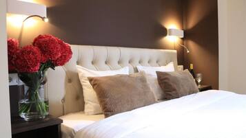 Een hotelkamer met een gestoffeerd hoofdeinde, een nachtkastje met een vaas rode bloemen en twee wandlampen.
