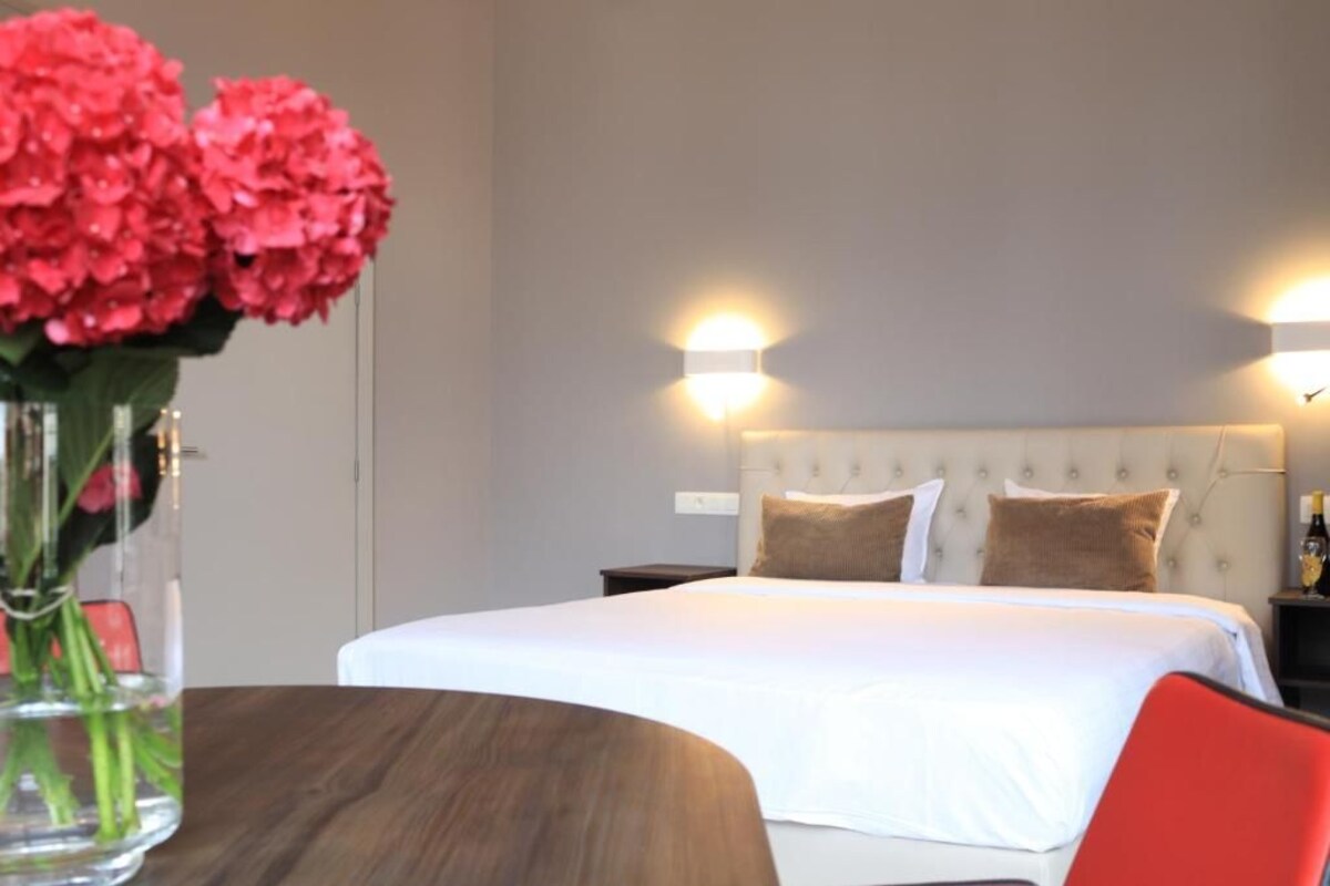 Et hotelværelse med en seng, natborde, en vase med blomster og vægmonterede lamper.