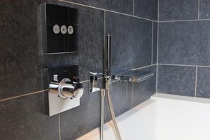 Et moderne badeværelse med et indbygget brusebad, en kromarmatur og en hylde med toiletartikler.