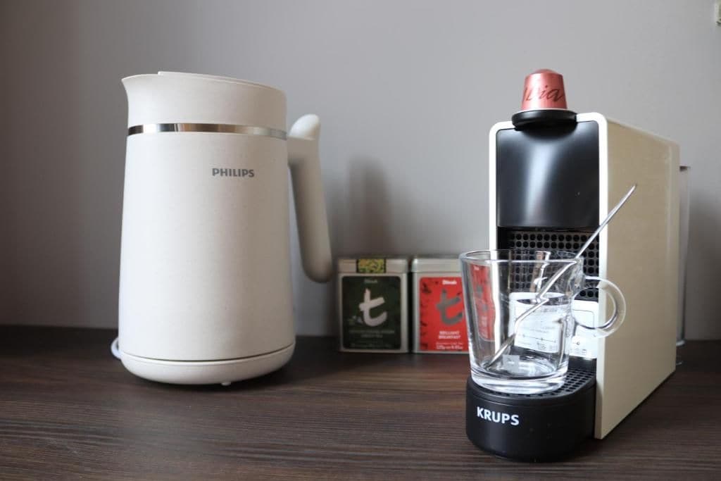 A coffee maker, a glass of water, and a box of tea on a wooden surface.