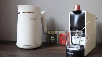 A coffee maker, a glass of water, and a box of tea on a wooden surface.