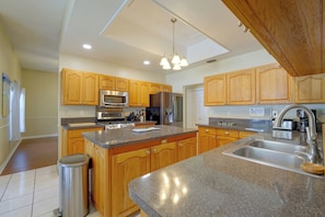 A kitchen with wooden cabinets, granite countertops, stainless steel appliances, and a trash can. - Private Outdoor Oasis! Palm Harbor Family Escape (Palm Harbor)