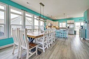 A modern kitchen with white cabinetry, a wooden dining table, and a teal accent wall. - Stroll to Beach! Family Surf City Home w/ Views (Holly Ridge)