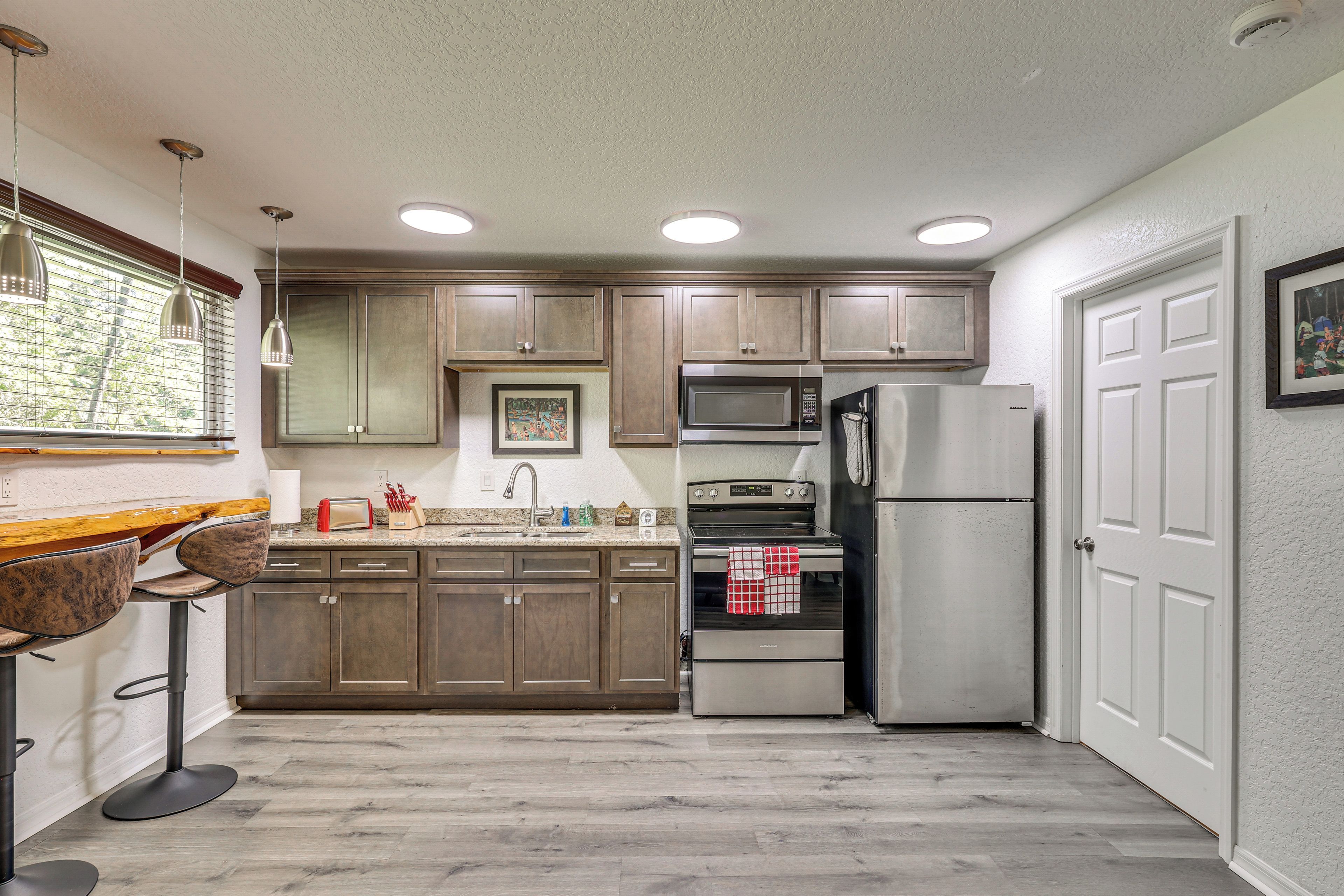 A kitchen with wooden cabinets, a stainless steel refrigerator, a microwave, an oven, and a sink.