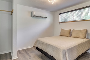 Un dormitorio con cama, ventana con persianas, equipo de aire acondicionado y suelo de madera.