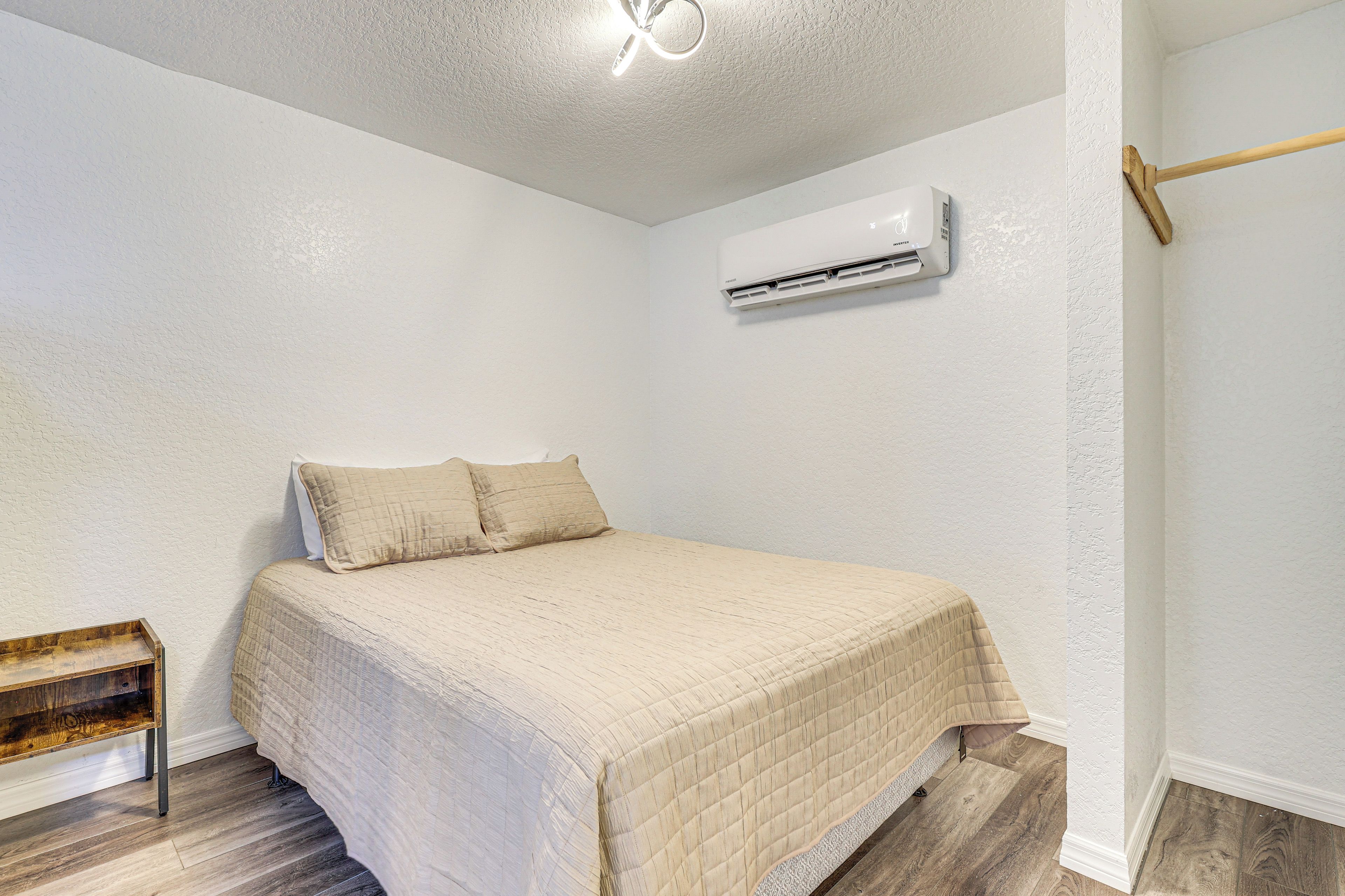 A bedroom with a bed, an air conditioning unit, a wooden bench, and a textured ceiling.