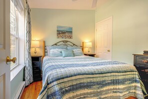 Quarto com cama, duas mesas de cabeceira com abajures, porta e janela com cortinas.
