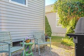A patio with two green chairs, a small table with a flower pot, and a barbecue grill. - Charming Coastal Getaway in Wells, Maine (Wells)