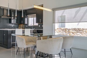 A modern kitchen with a glass dining table and four chairs, a built-in oven, and a large window with a stone wall view. - 8 Mi to the Franklins: Modern Home w/ Mtn Views! (El Paso)