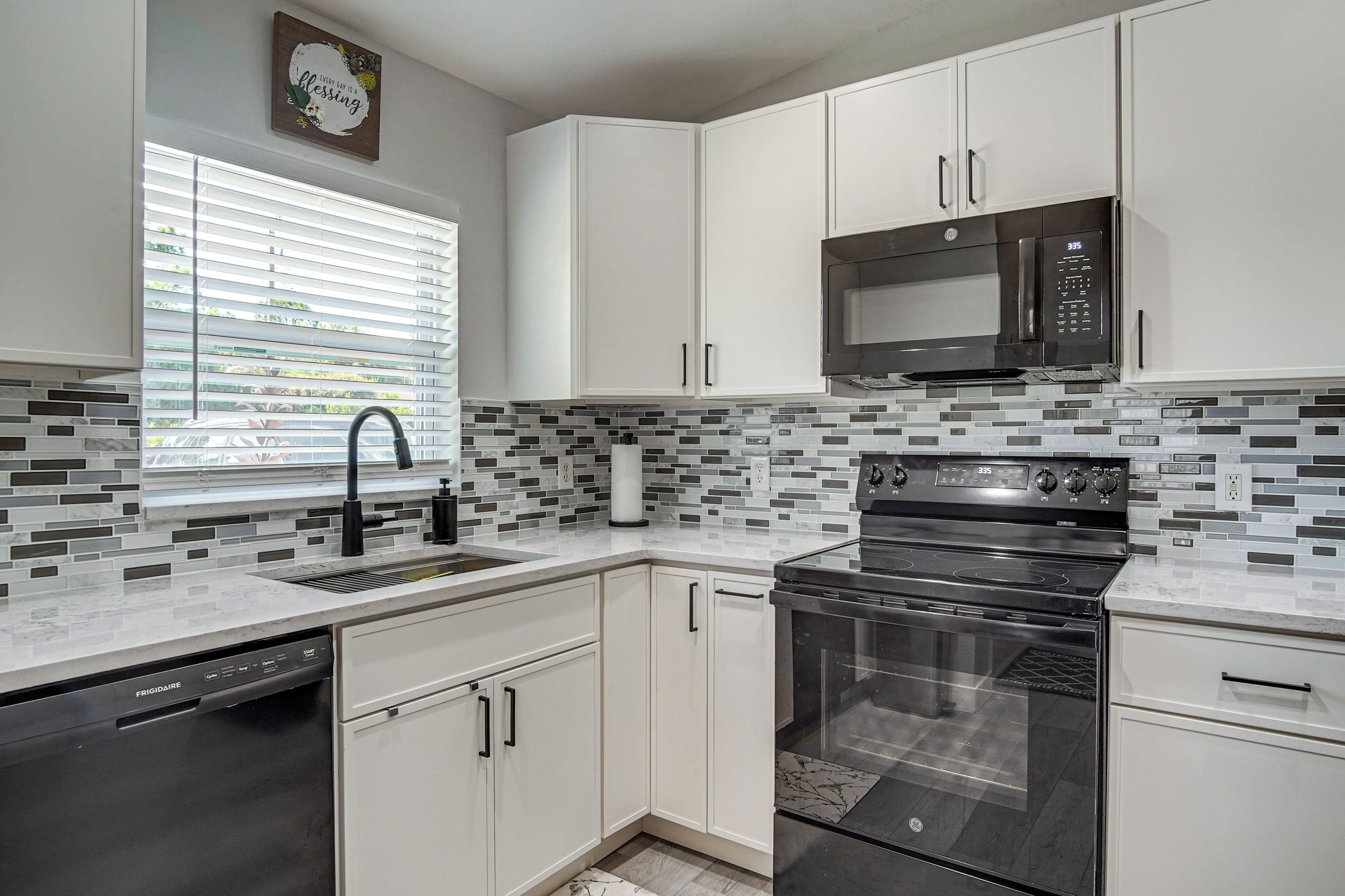 A modern kitchen with white cabinets, a black microwave, and a stainless steel oven.
