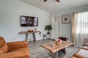 A living room with a television mounted on the wall, a coffee table with books and flowers, a sofa, and a decorative plant.