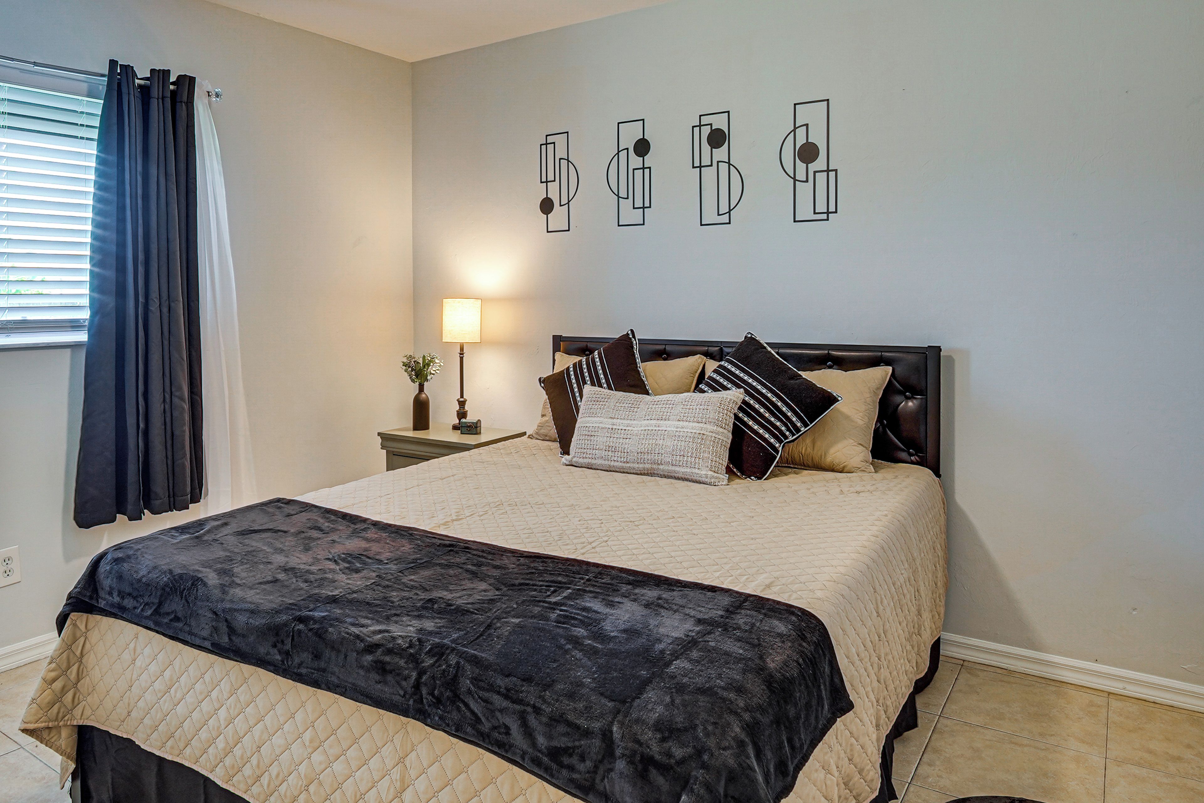 A bedroom with a bed, a nightstand, a lamp, and a window with curtains.
