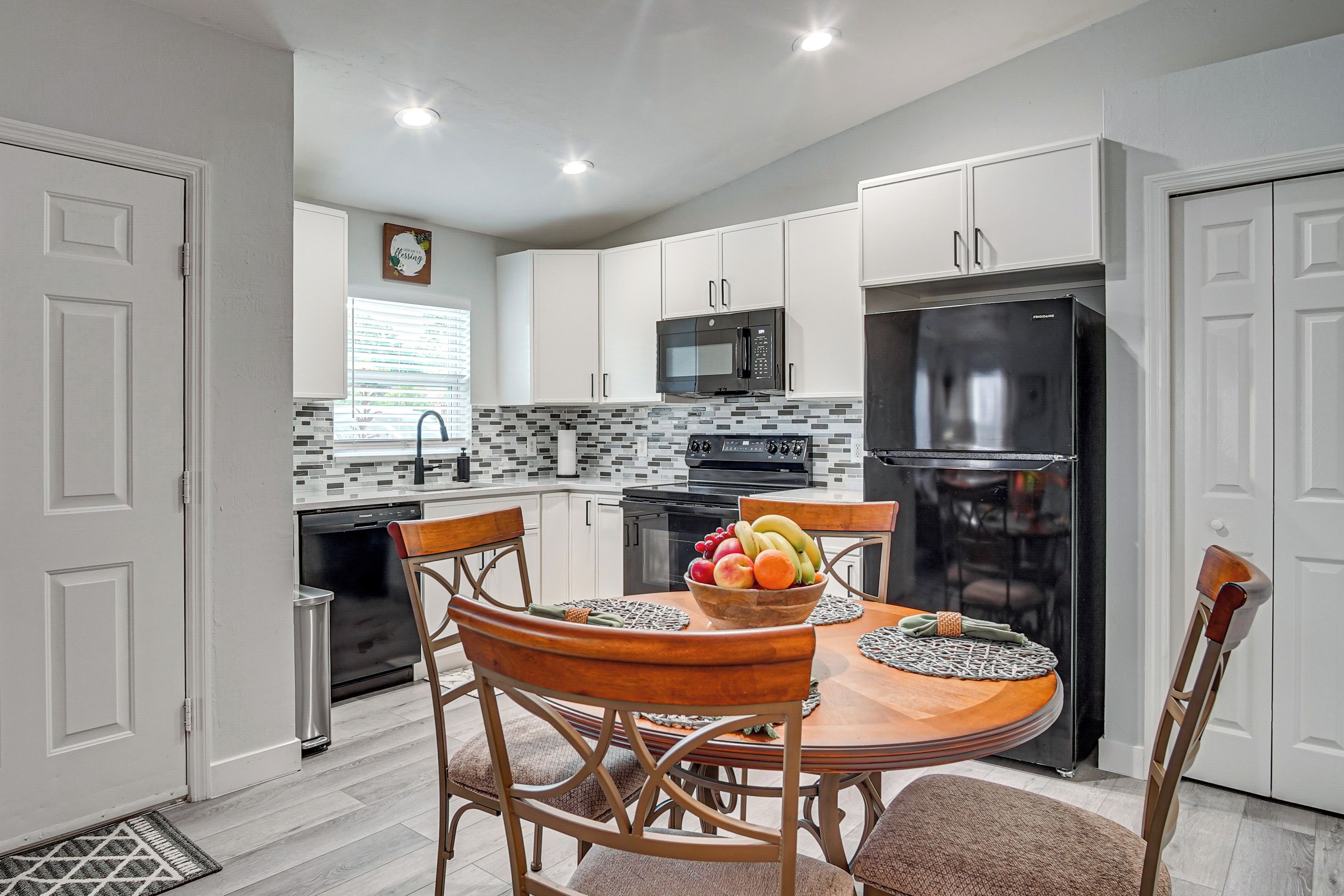 A modern kitchen with white cabinets, a black refrigerator, and a dining table with chairs.