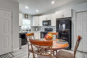 A modern kitchen with white cabinets, a black refrigerator, and a dining table with chairs.