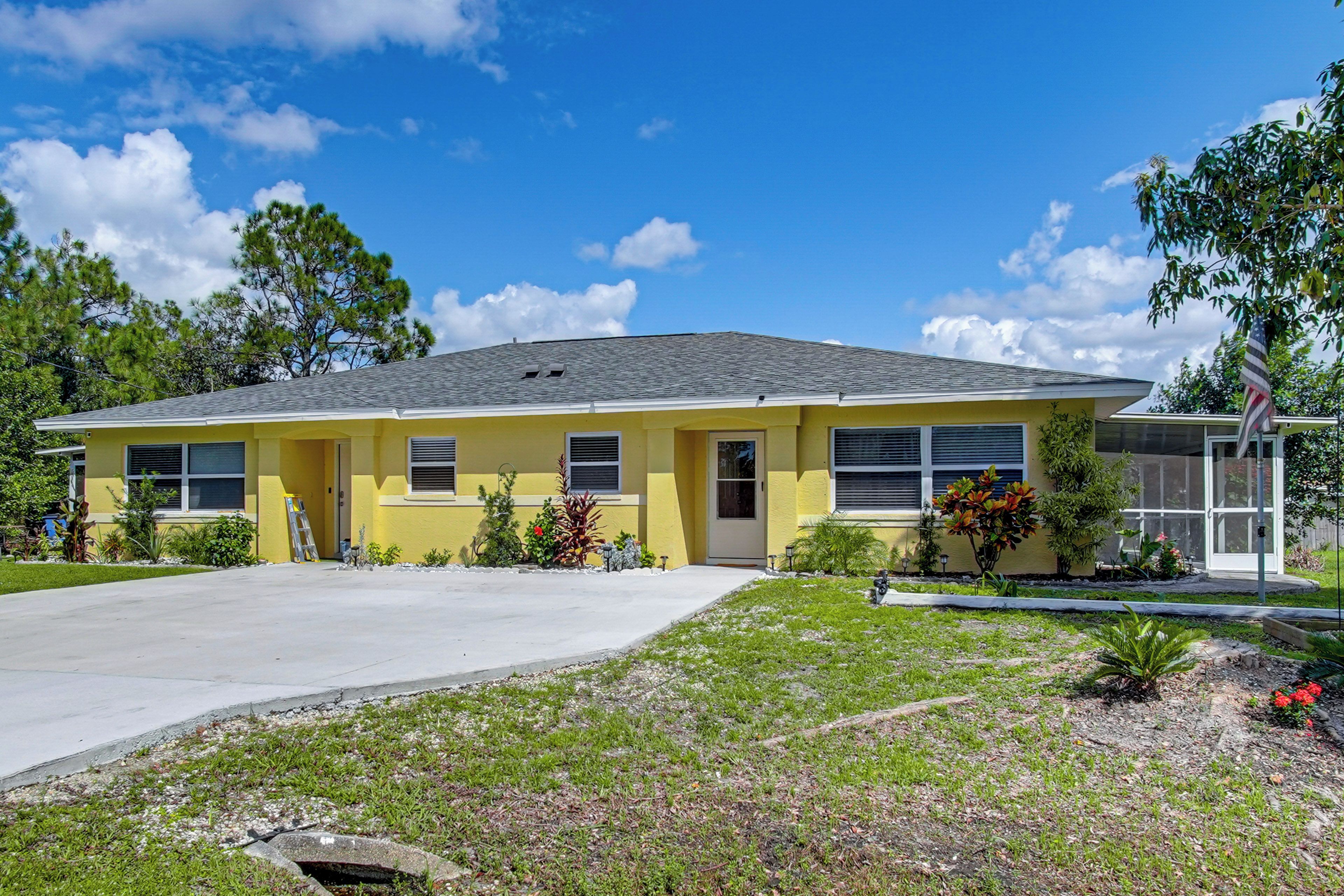 A yellow single-story house with a front porch, a driveway, and a well-maintained lawn.