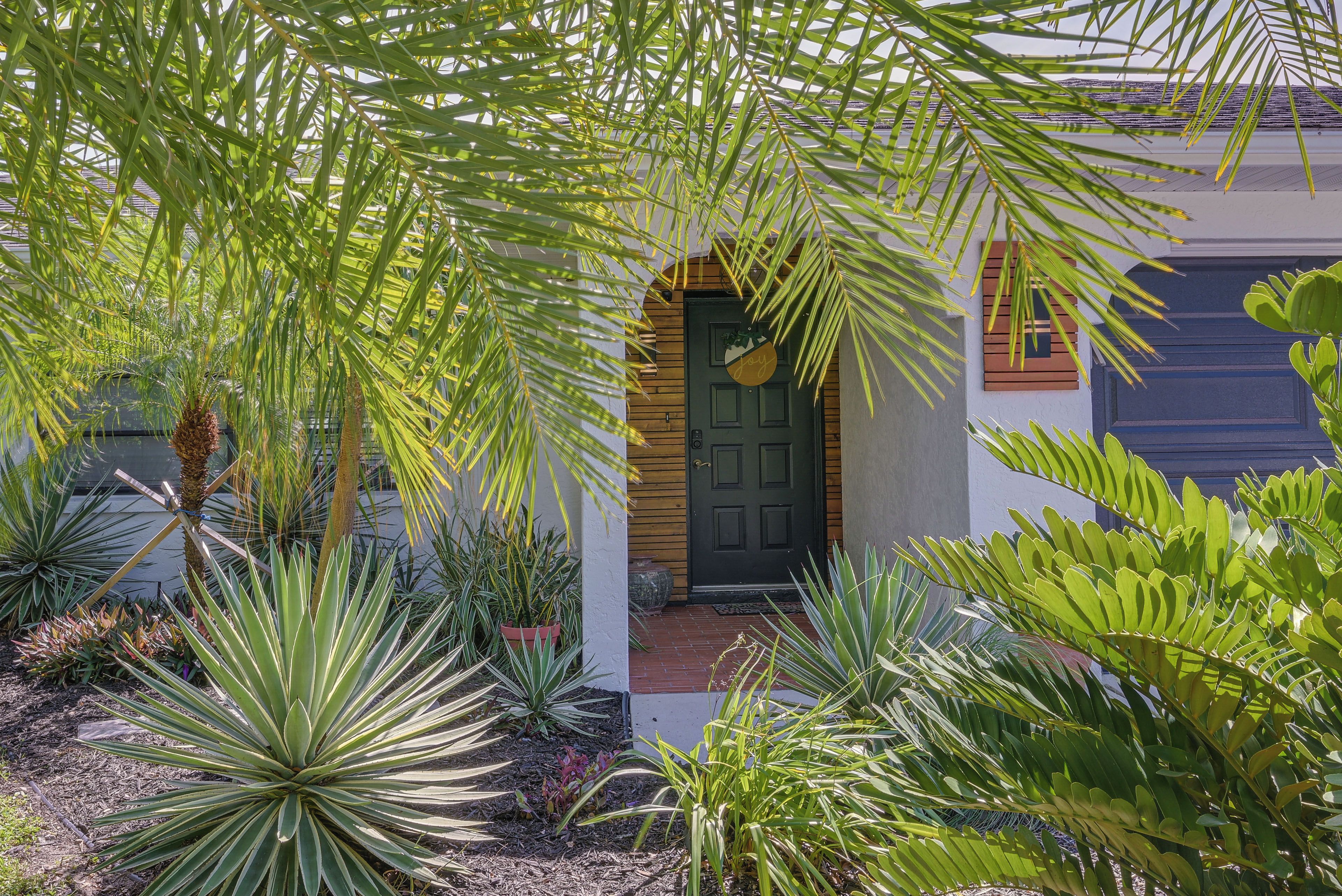 A house with a dark front door, surrounded by various plants and a small porch area.