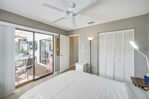 A bedroom with a bed, a ceiling fan, a nightstand, a lamp, and a sliding glass door leading to a patio. - Heated Pool, Fishing Dock! Florida Escape on Canal (Port Charlotte)