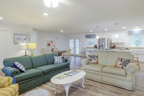 A spacious living room with a green sofa, a beige sofa, and a white coffee table. There is a dining area with a table and chairs in the background. - Beaufort Home Near Fishing & Historic Waterfront (Beaufort)