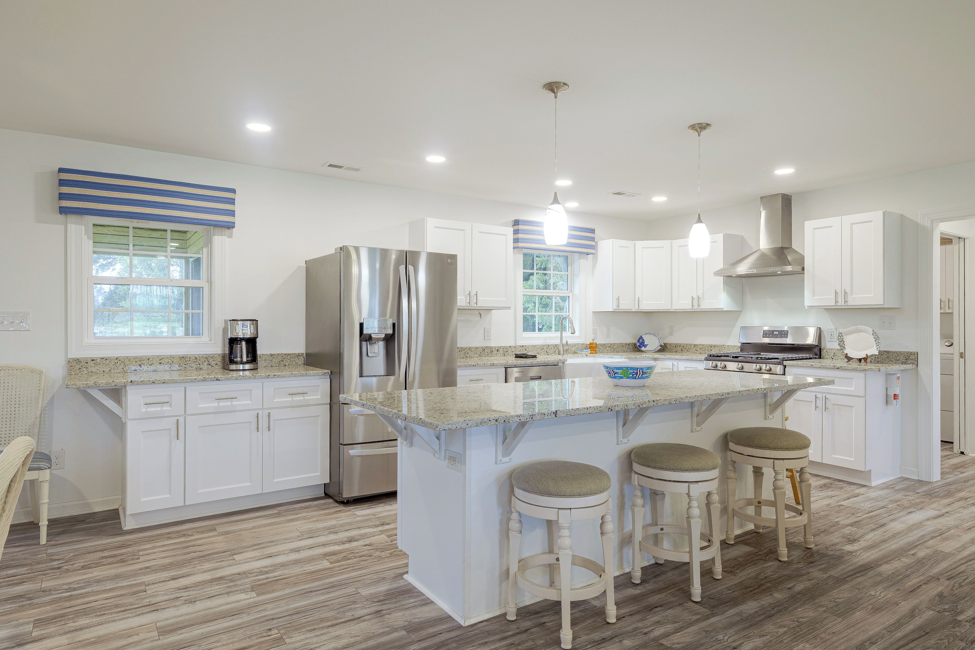 A modern kitchen with white cabinets, stainless steel appliances, a granite countertop, and a central island with bar stools.