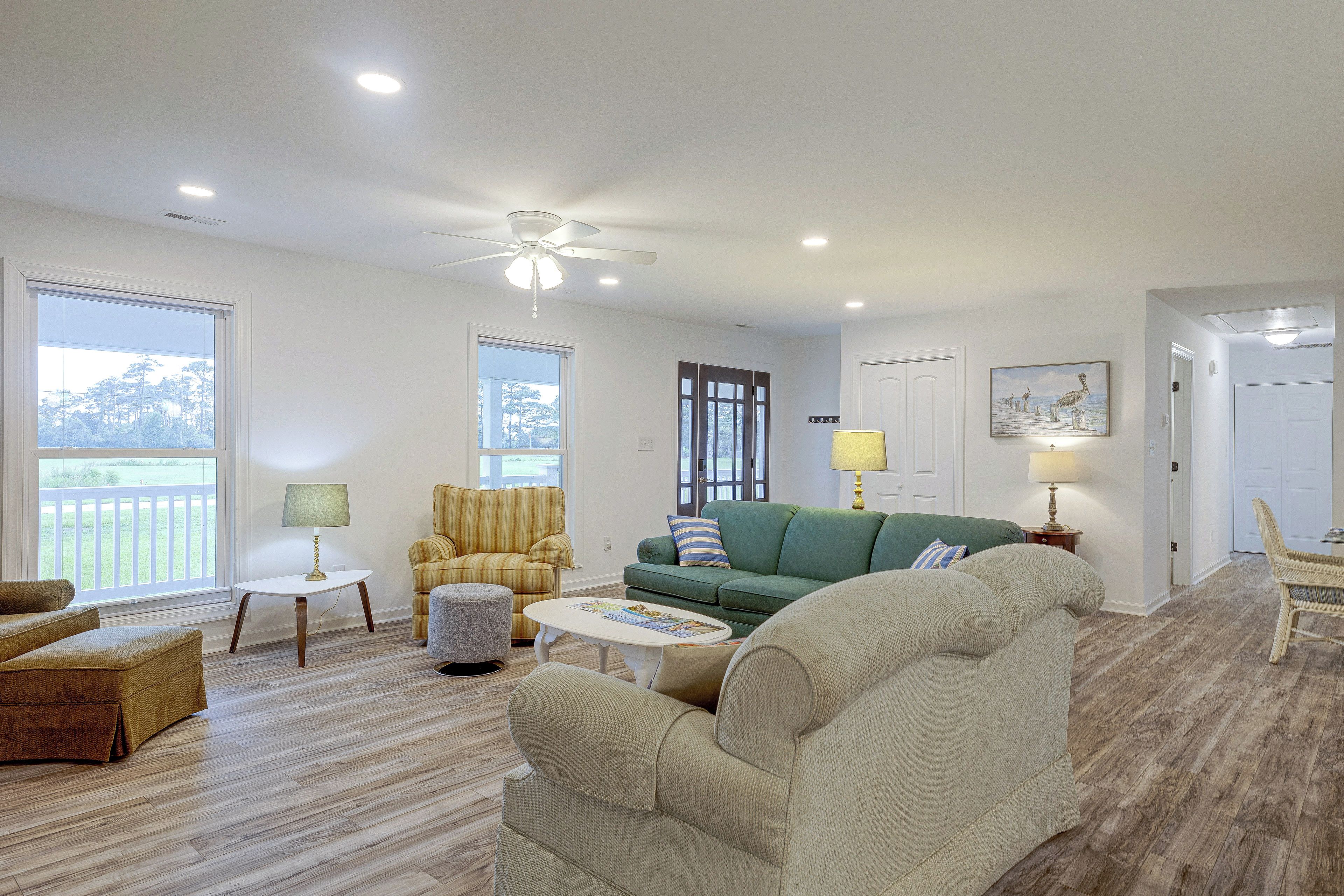A spacious living room with a ceiling fan, large windows, and a view of a deck.
