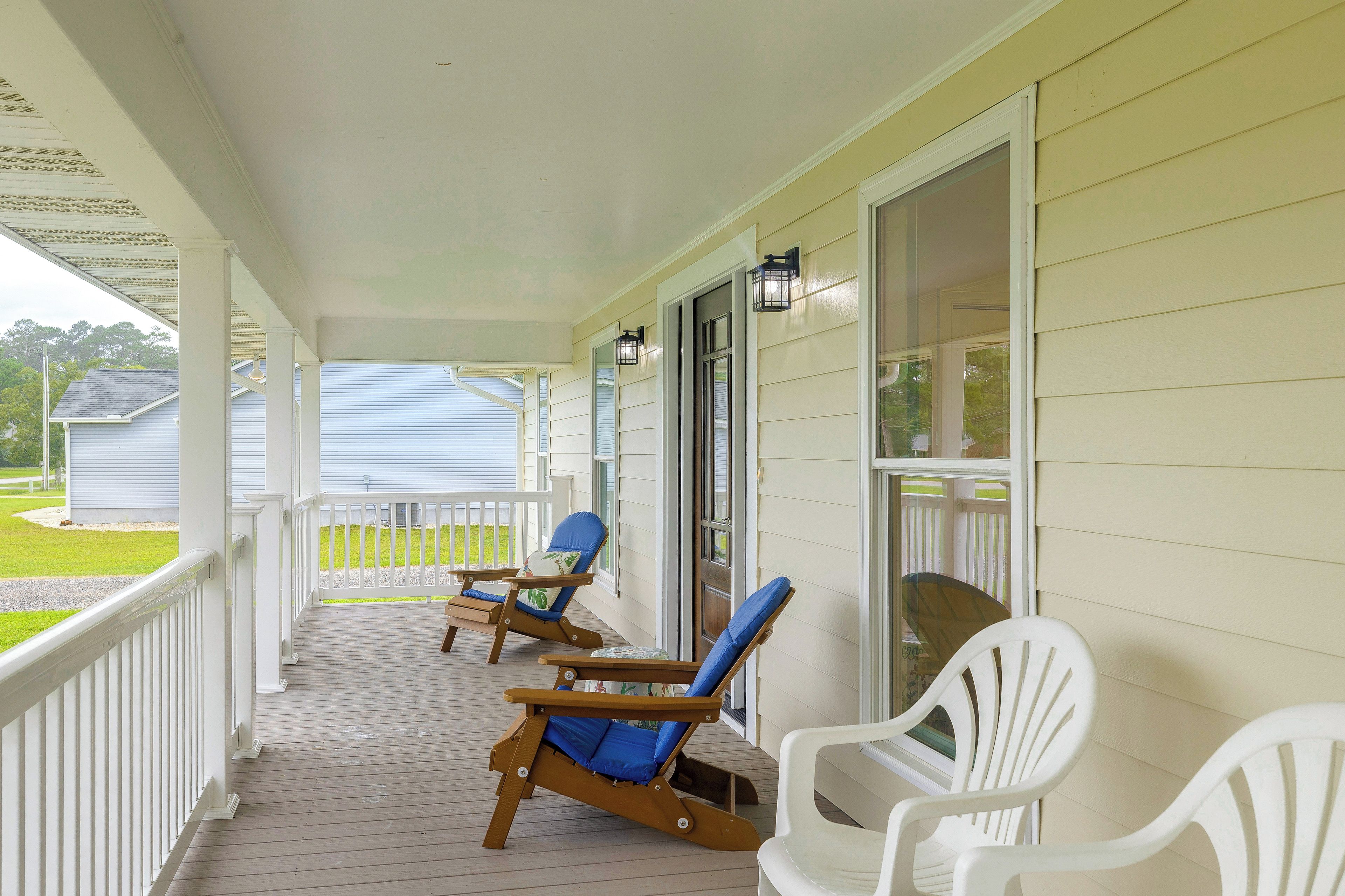 A covered porch with two wooden rocking chairs and a white plastic chair.