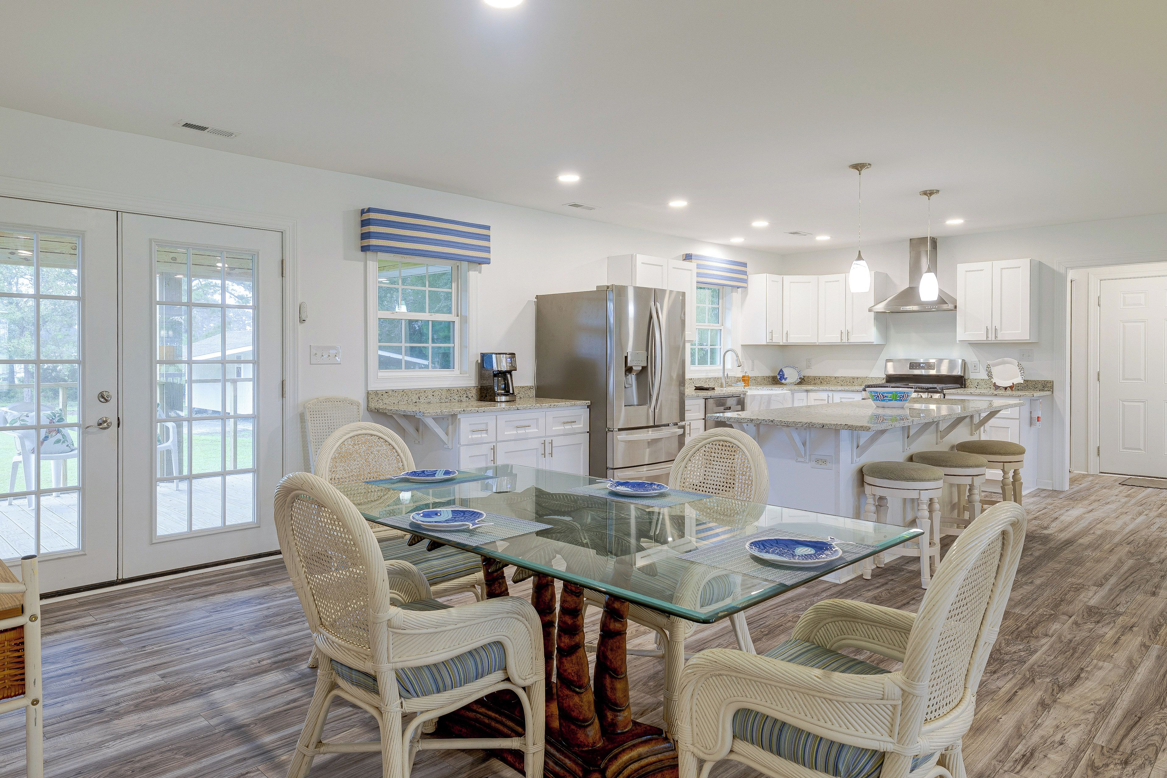 A modern kitchen with white cabinetry, a glass dining table, wicker chairs, and a view through the glass doors.