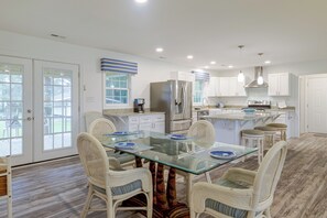 A modern kitchen with white cabinetry, a glass dining table, wicker chairs, and a view through the glass doors. - Beaufort Home Near Fishing & Historic Waterfront (Beaufort)