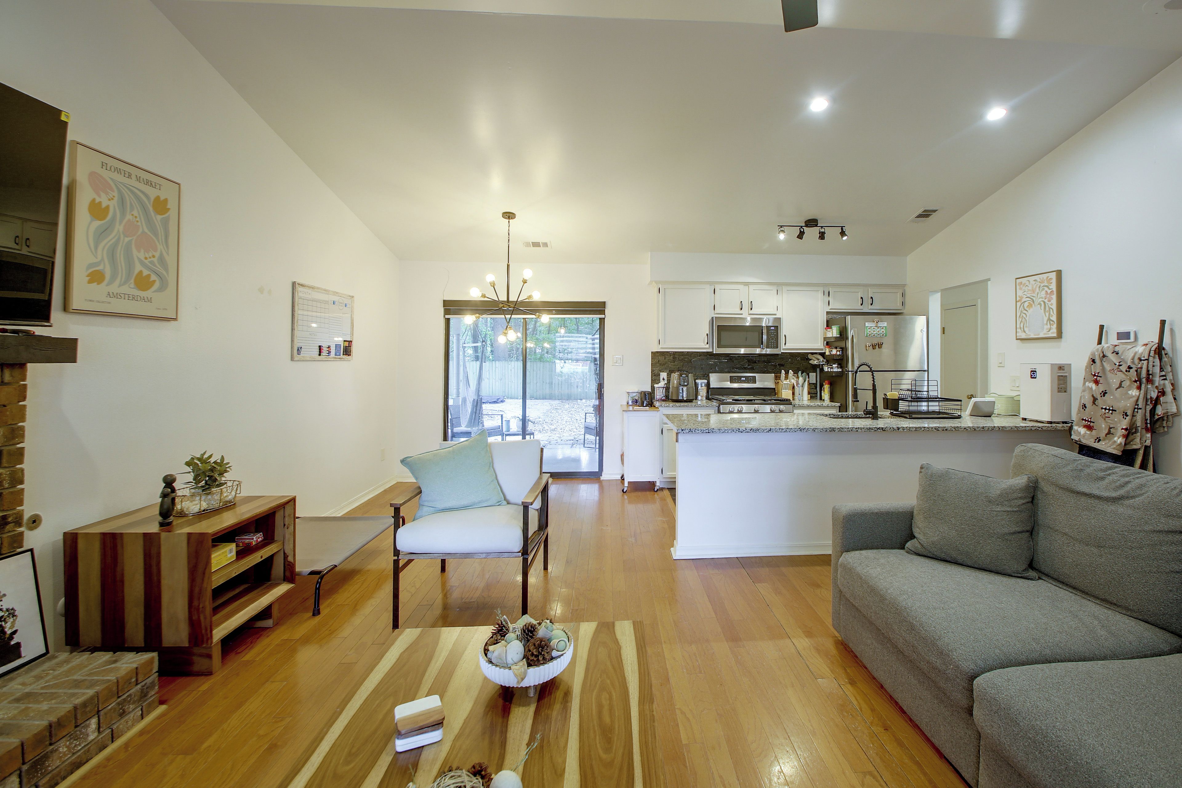 Una cocina moderna con electrodomésticos de acero inoxidable, un comedor con mesa y sillas de madera, y una sala de estar con un sofá gris.