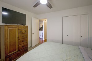 Ein Schlafzimmer mit einem Bett, einer Holzkommode, einem an der Wand befestigten Fernseher und einer Tür zu einem Badezimmer.