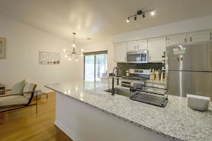 Uma cozinha moderna com bancadas de granito, eletrodomésticos de aço inoxidável e uma área de jantar com cadeira e mesa.