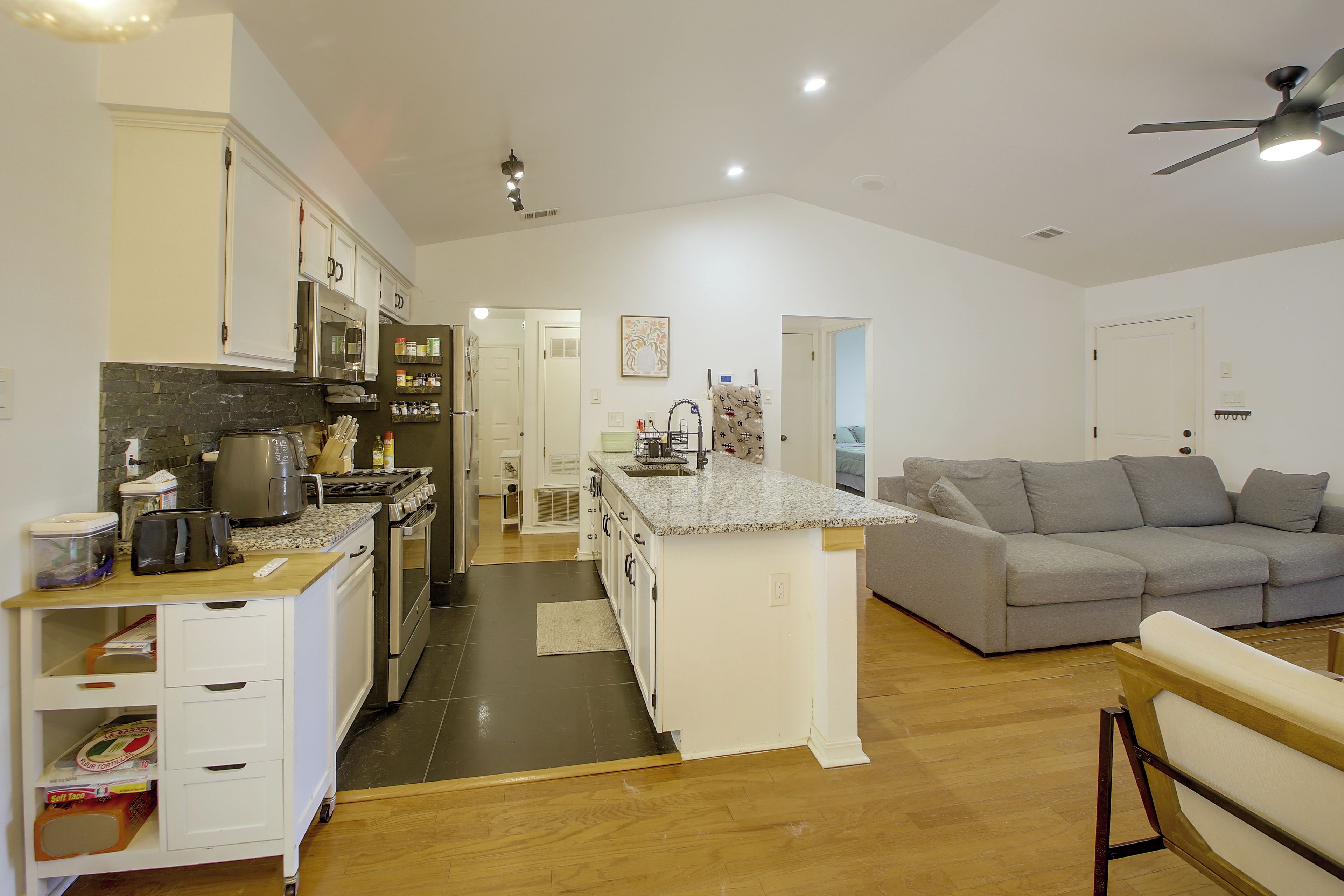 Una cocina moderna con una isla central, un sofá gris y un ventilador de techo.