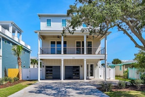 A two-story house with a balcony, garage doors, and a clear driveway. - 🌊Ocean Blvd Retreat at the Beach: Newly Built 5Br🏖️ (Carolina Beach)