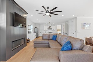 A modern living room with a sectional sofa, a fireplace, and a ceiling fan. - 🌊Ocean Blvd Retreat at the Beach: Newly Built 5Br🏖️ (Carolina Beach)