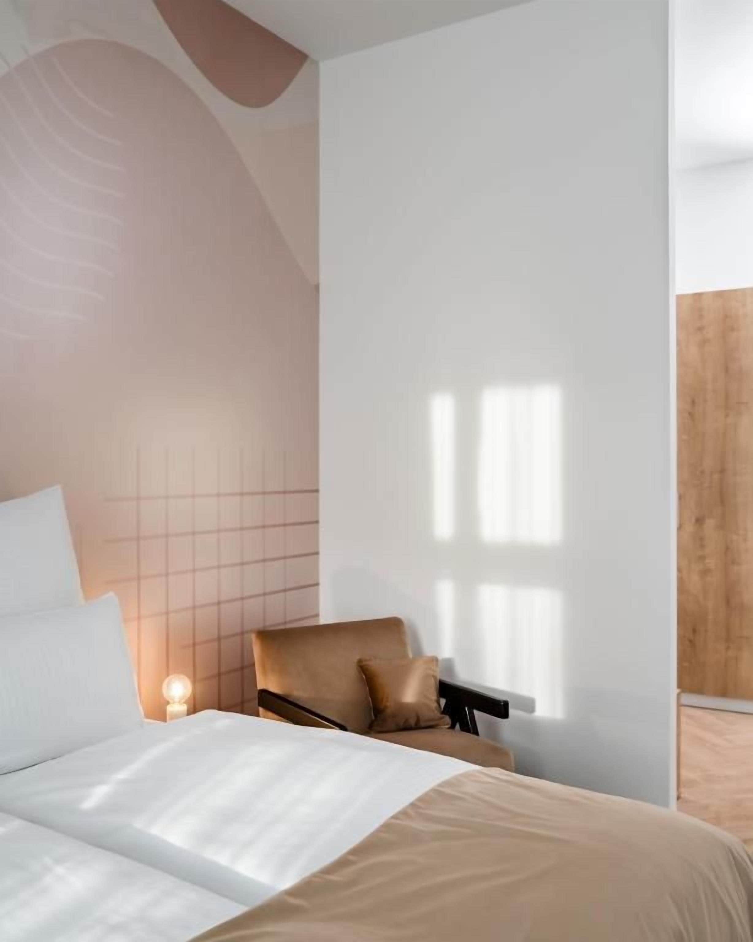 Ein modernes Hotelzimmer mit einem Bett, einem Sessel und einem Nachttisch mit Lampe.
