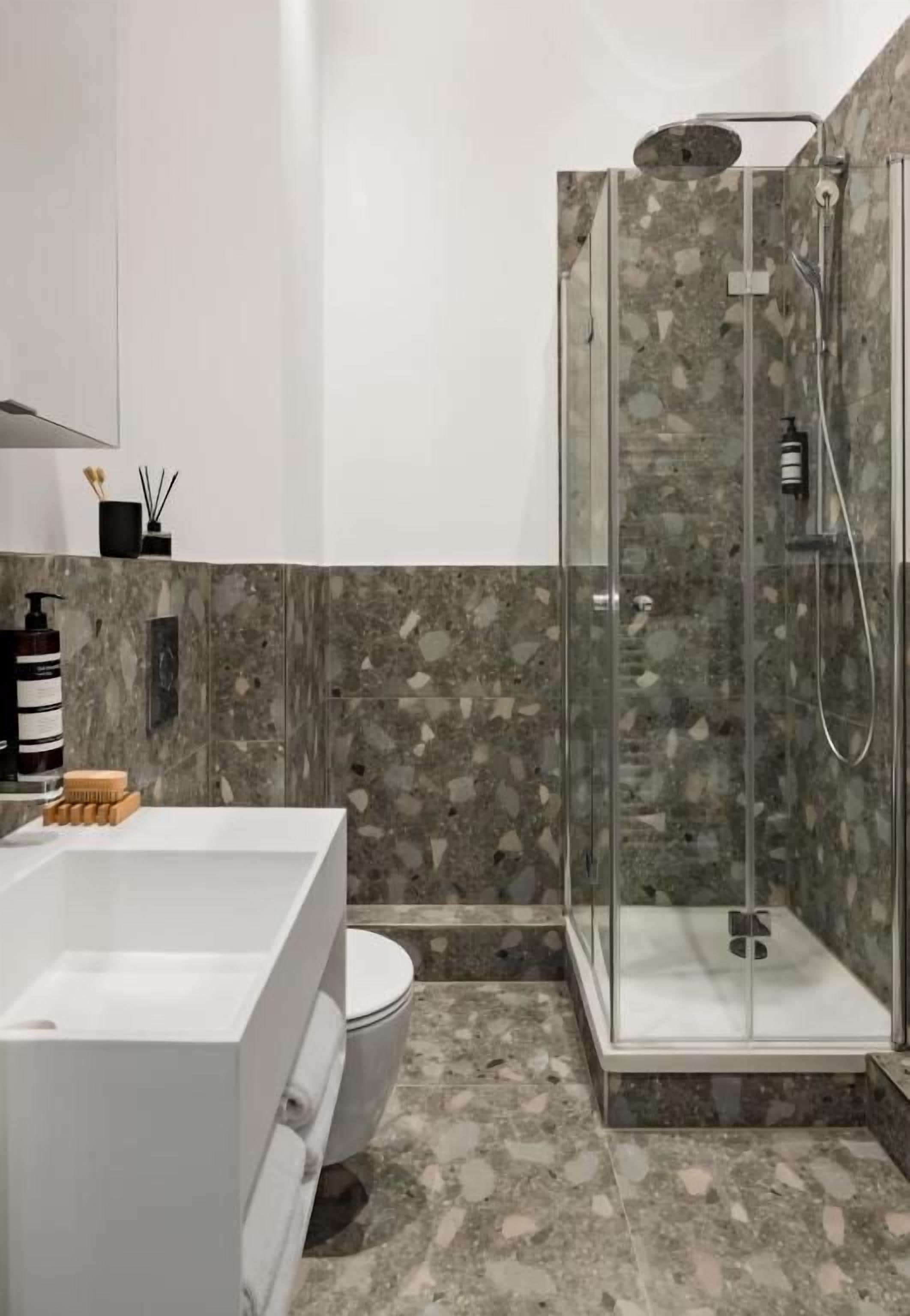 A modern bathroom with a glass-enclosed shower, a white bathtub, and a marble-tiled floor.