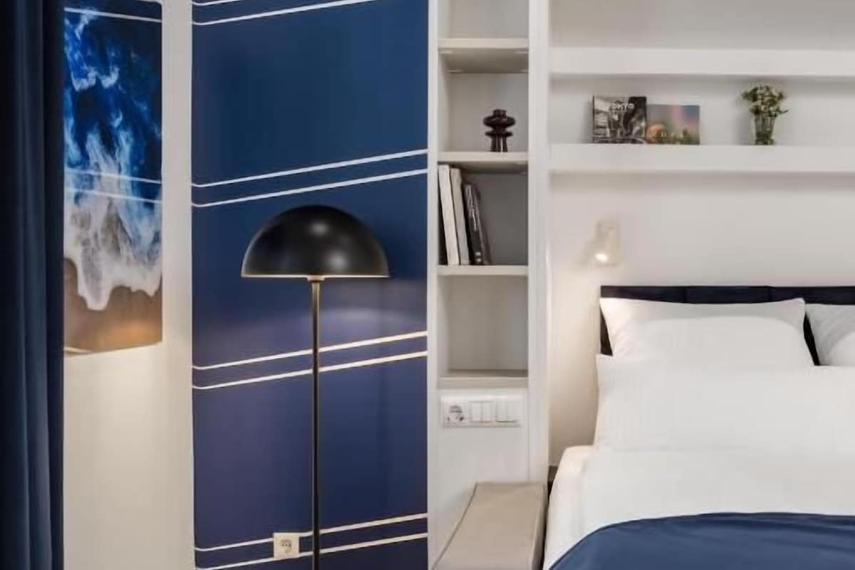 Un dormitorio con cama, mesita de noche, lámpara de pie y estantería.