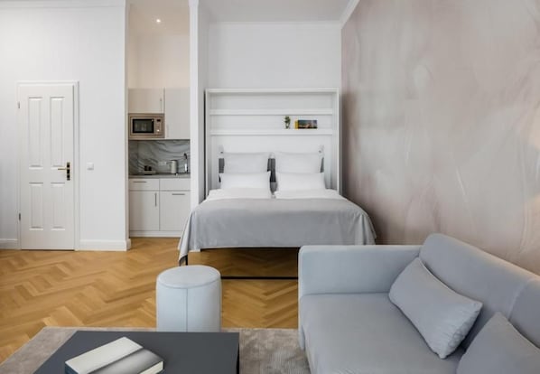 A modern bedroom with a bed, a sofa, a small table, and a kitchenette. - FU Life Berlin Kudamm (Berlin)