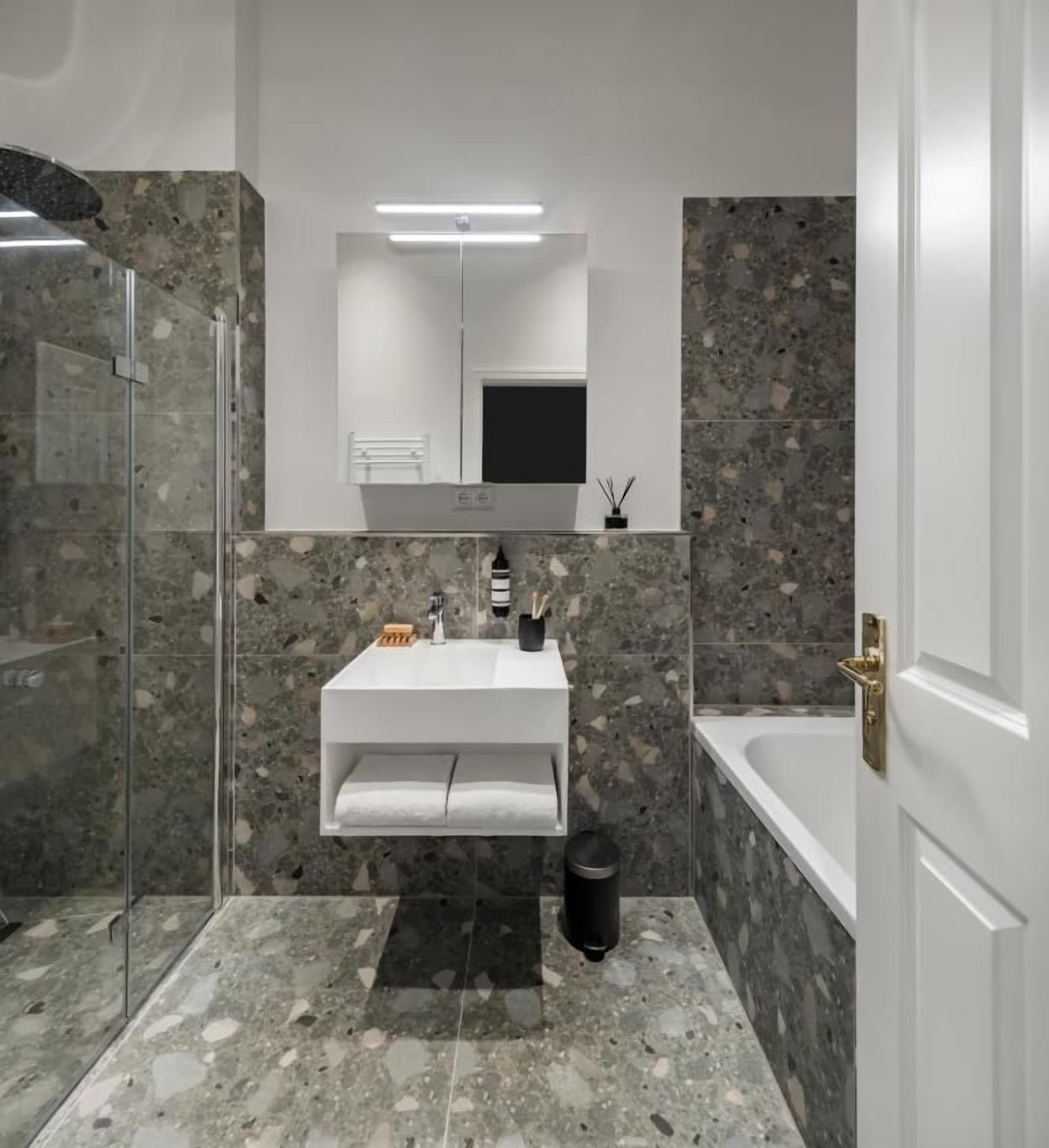 Une salle de bain moderne avec une douche à parois de verre, un lavabo blanc avec un miroir au-dessus et une baignoire.