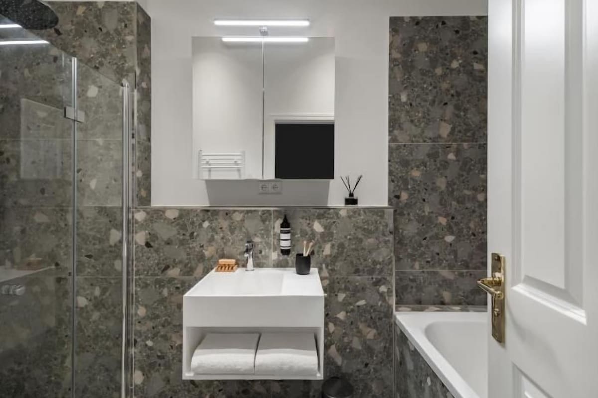 Un baño moderno con cabina de ducha de vidrio, un lavabo blanco con espejo y una bañera.