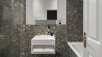 Une salle de bain moderne avec une douche à parois de verre, un lavabo blanc avec un miroir au-dessus et une baignoire.
