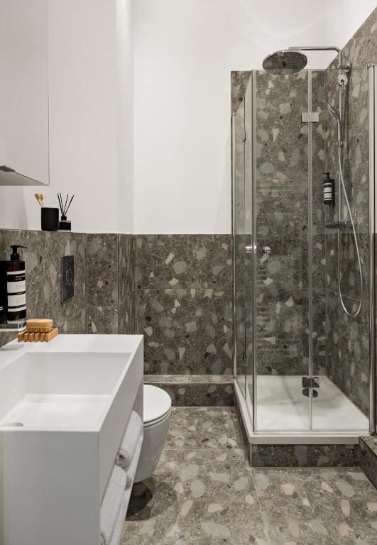 A modern bathroom with a glass-enclosed shower, a white bathtub, and a marble-tiled floor.