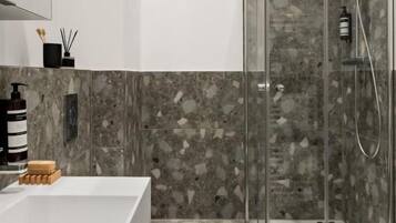 A modern bathroom with a glass-enclosed shower, a white bathtub, and a marble-tiled floor.