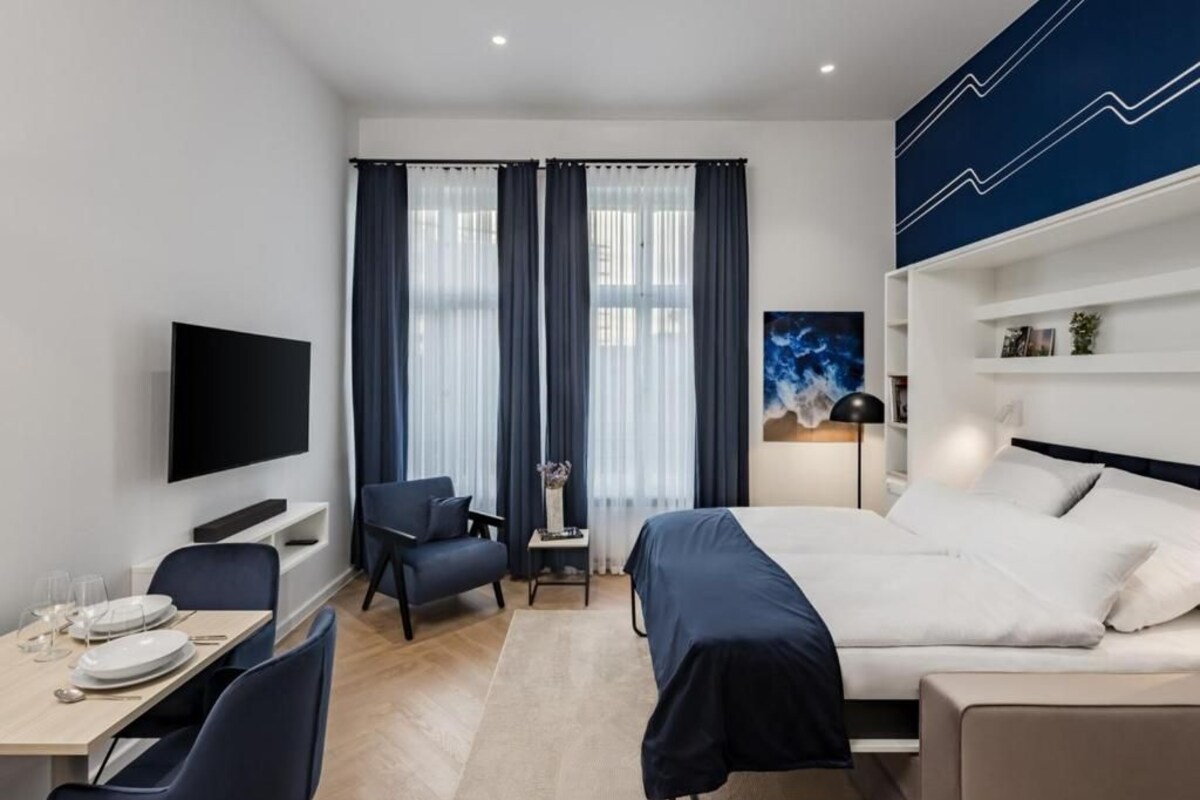 Una habitación de hotel moderna con cama, escritorio, silla, televisor y ventana con cortinas.