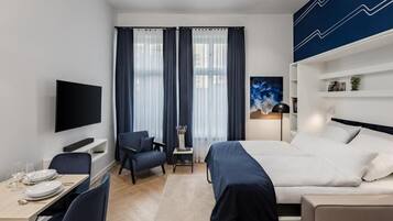 Una habitación de hotel moderna con cama, escritorio, silla, televisor y ventana con cortinas.