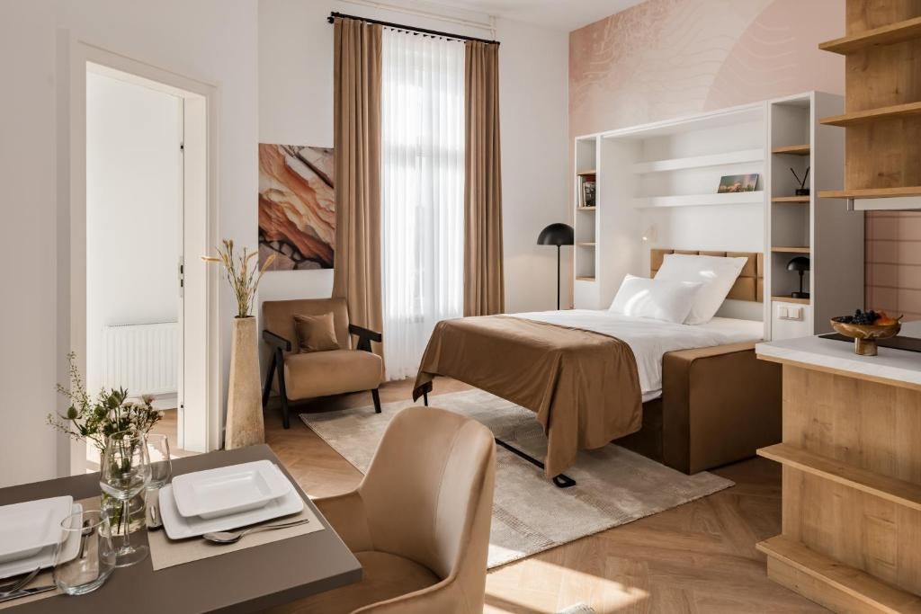 A hotel room with a bed, a chair, a desk with a vase of flowers, and a bookshelf.